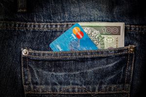Banknot 100 zł i karta płatnicza wystająca z kieszeni dżinsowych spodni
