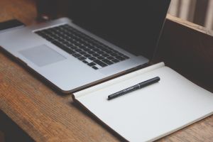 laptop i zeszyt z długopisem na biurku