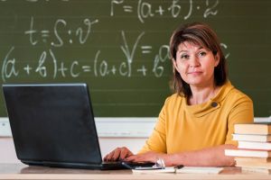 Nauczycielka z laptopem i książkami znajdującymi się na biurku.