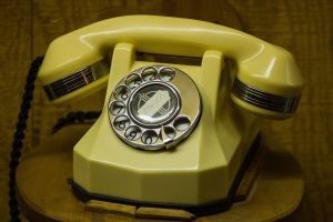 Żółty telefon stacjonarny znajdujący się na drewnianym stole