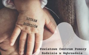 Rączka dziecka położona na ręce osoby dorosłej. Na rączce dziecka napis SZUKAM RODZICÓW.