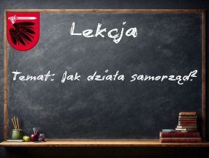 Tablica szkolna, na której znajduje się herb Powiatu Wąbrzeskiego oraz temat lekcji: Jak działa samorząd?