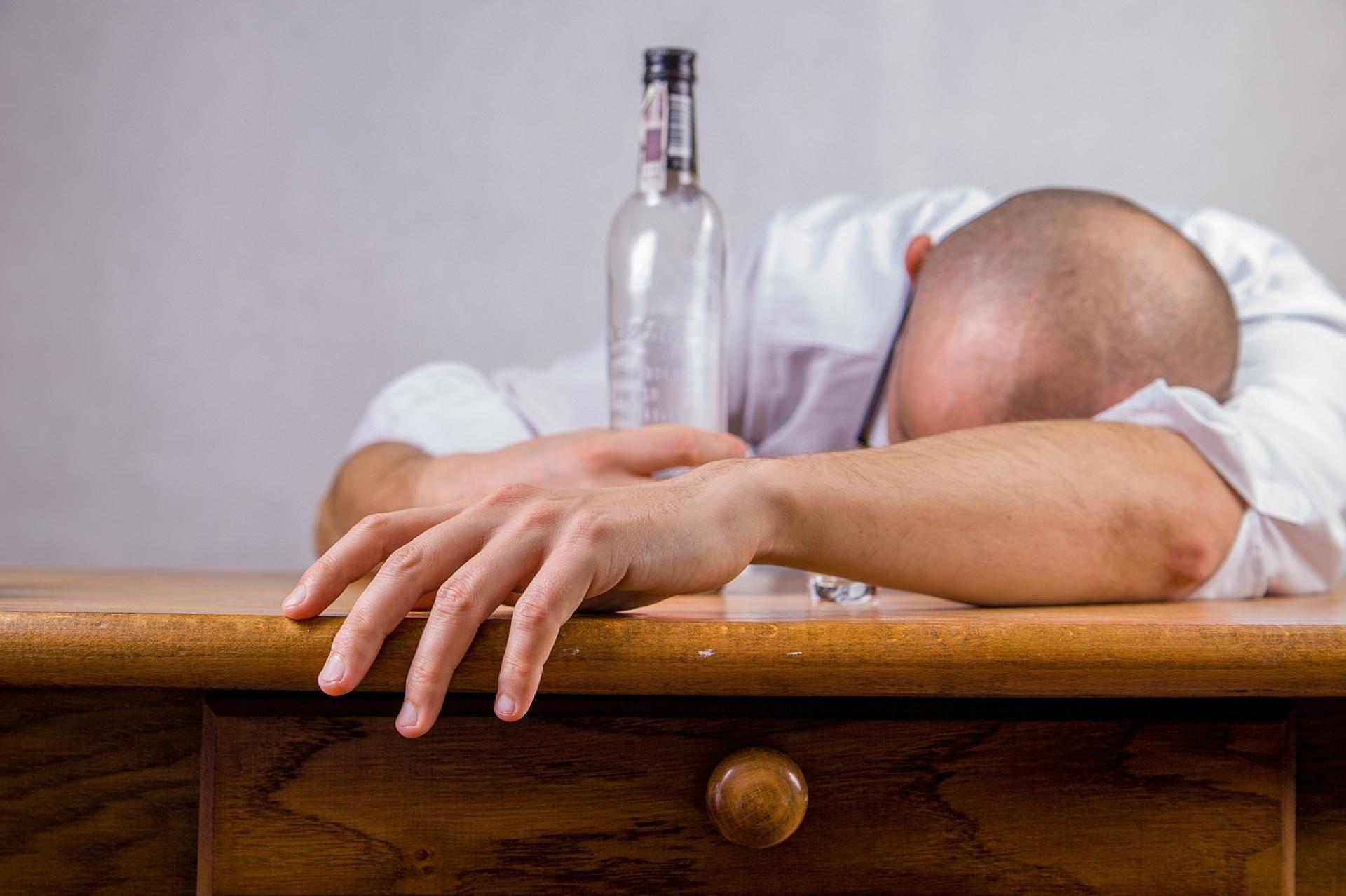 mężczyzna leżący na stole z pustą butelką po alkoholu